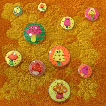 Les badges Chatpignon débarquent ! Illustrés à la main et enfermés dans un badge en plastique transparent, ils se déclinent en 3 tailles (mini, médium, maxi). Des couleurs fluo qui brillent sous lumière bleue pour un effet magique ✨. À épingler partout : veste, sac, casquette… ou à collectionner comme de vraies pépites. Collection limitée, fun et décalée